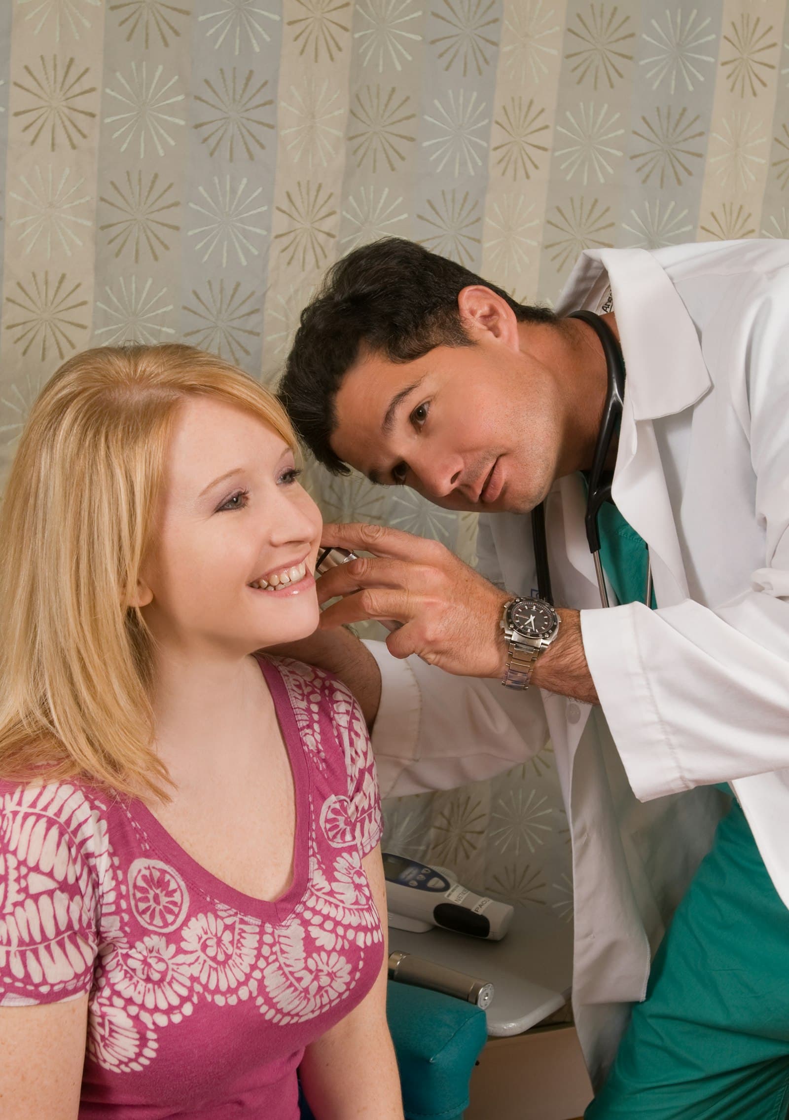 A doctor examining a smiling patient's ear with an otoscope